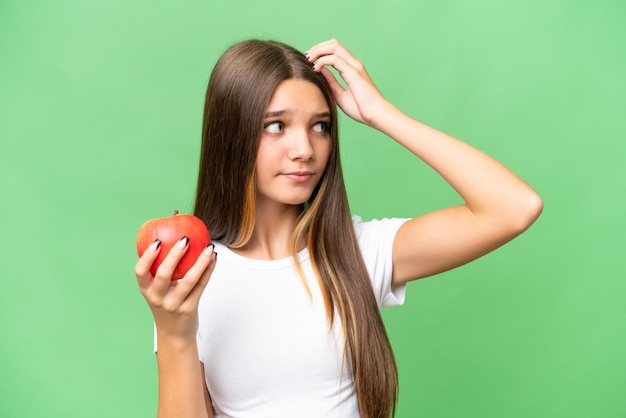 Ragazza caucasica dell'adolescente che tiene una mela sopra priorità bassa isolata che ha dubbi e con espressione del viso confusa