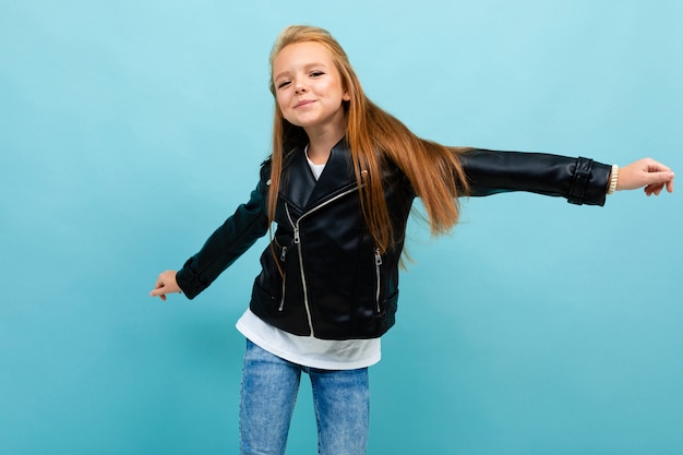 Ragazza caucasica dell'adolescente nei sorrisi neri dei jeans e del rivestimento isolati sull'azzurro