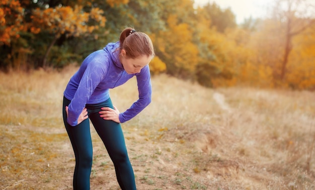 Ragazza caucasica esaurita del pareggiatore in camicia blu e leggins sportivi neri che riposa dopo il jogging