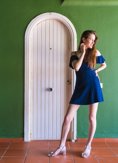 Ragazza caucasica in un vestito blu accanto a una porta bianca di una foto verticale della casa verde