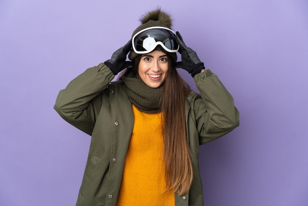 Ragazza caucasica sciatore con occhiali da snowboard isolato sulla parete viola con espressione di sorpresa