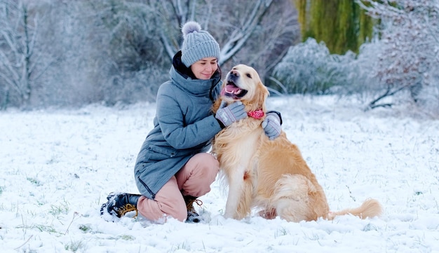 Ragazza che abbraccia il suo bel cane golden retriever all'aperto sulla neve in inverno