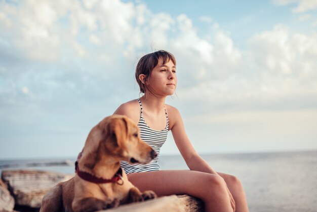 Ragazza che abbraccia il suo cane mentre era seduto sulla roccia in riva al mare