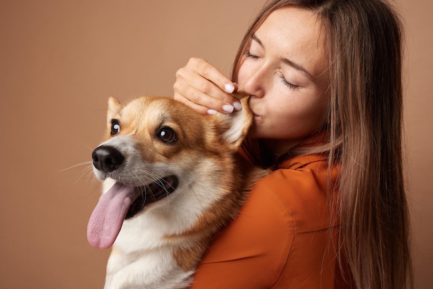 Ragazza che abbraccia un Pembroke Welsh Corgi su uno sfondo beige pulito nello studio amore per gli animali