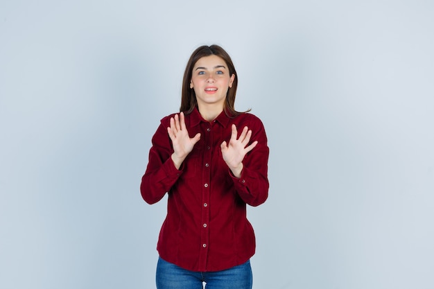 Ragazza che alza le mani in modo protettivo in camicetta bordeaux e sembra preoccupata