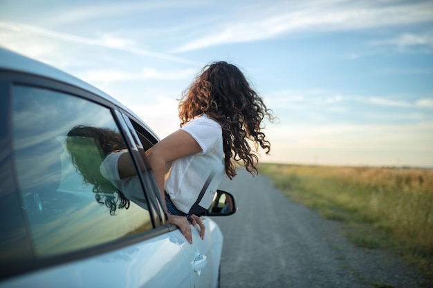 Ragazza che attacca il suo corpo fuori dal finestrino di un'auto. Concetto di libertà e avventura.