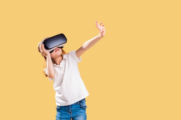 Ragazza che avverte il gioco della cuffia avricolare di VR su giallo. Emozioni sorprese sul suo viso. Bambino usa un gadget di gioco per la realtà virtuale.