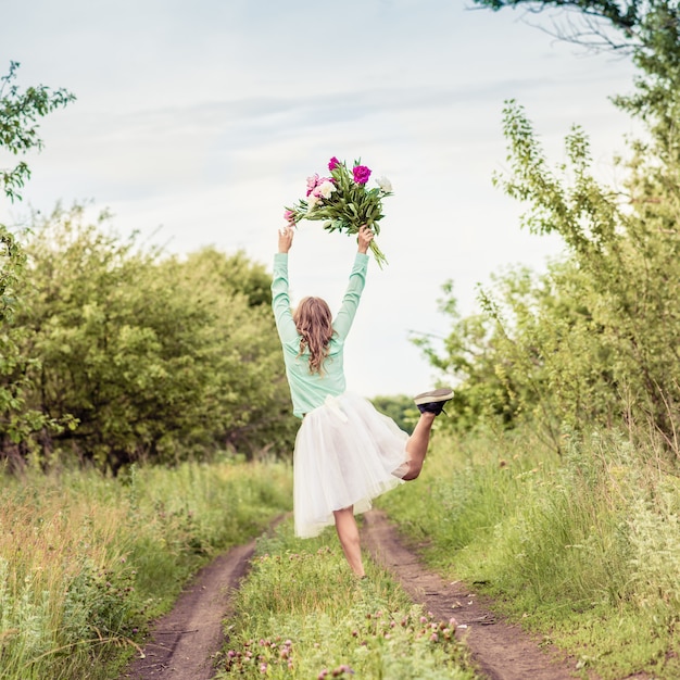 Ragazza che balla in natura con un mazzo di fiori