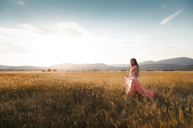 Ragazza che balla in un campo con un bel vestito rosa al tramonto