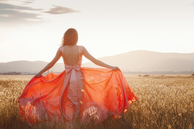 Ragazza che balla in un campo con un bel vestito rosa al tramonto