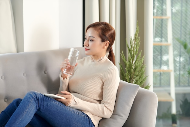 Ragazza che beve acqua seduta su un divano a casa