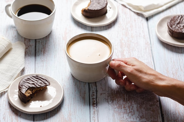 Ragazza che beve caffè e mangia cioccolato alfajores su un tavolo di legno