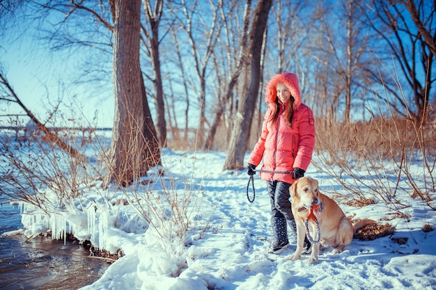 Ragazza che cammina con il suo labrador retriever giallo nel paesaggio invernale