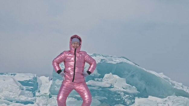 Ragazza che cammina sul ghiaccio incrinato del lago ghiacciato Baikal Donna viaggiatore esplora e guarda un lastrone di ghiaccio Luogo magico più puro della natura Il ghiaccio circonda il viaggiatore per tutto il suo viaggio Escursionista cammina in giacca rosa cosmica