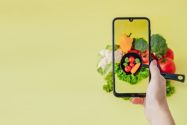 Ragazza che cattura maschera di alimento vegetariano sulla tabella con il suo smartphone. Vegan e concetto sano.