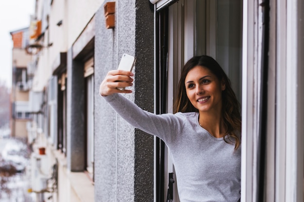 Ragazza che cattura selfie a una finestra aperta