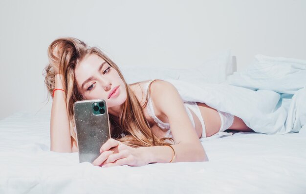 Ragazza che chiacchiera al telefono la mattina a letto donna a letto che controlla le app social con lo smartphone