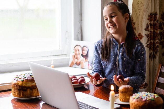 Ragazza che dimostra le uova e saluta con le vacanze primaverili la sua famiglia via Internet, la celebrazione del mangiatore online, la nuova distanza normale e sociale.