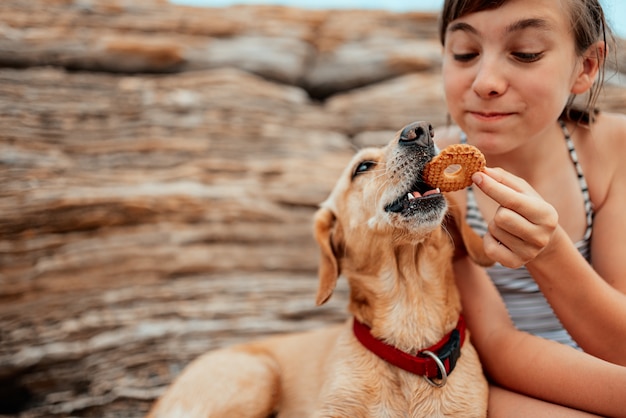 Ragazza che divide i biscotti con il suo cane sulla spiaggia