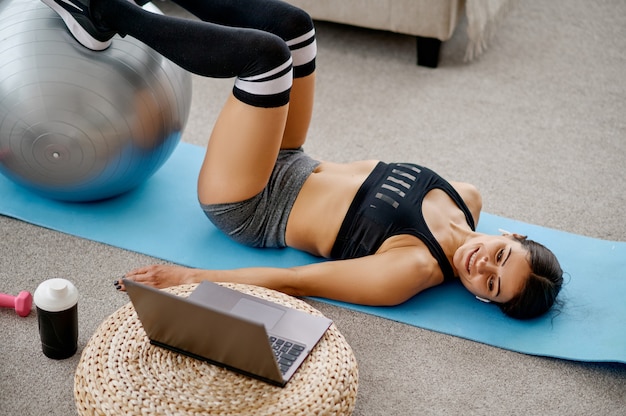 Ragazza che fa esercizio con la palla, formazione online di pilates al computer portatile