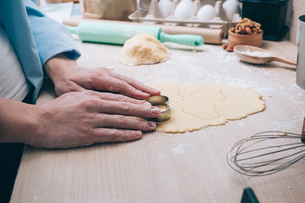 Ragazza che fa i biscotti a forma di cuore in cucina, primo piano. Sorpresa per i tuoi cari a San Valentino, festa della mamma o festa del papà. Sfondo culinario festivo, con amore.