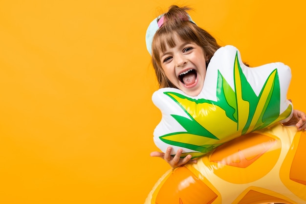 Ragazza che fa smorfie con un anello di gomma di ananas su uno sfondo giallo.