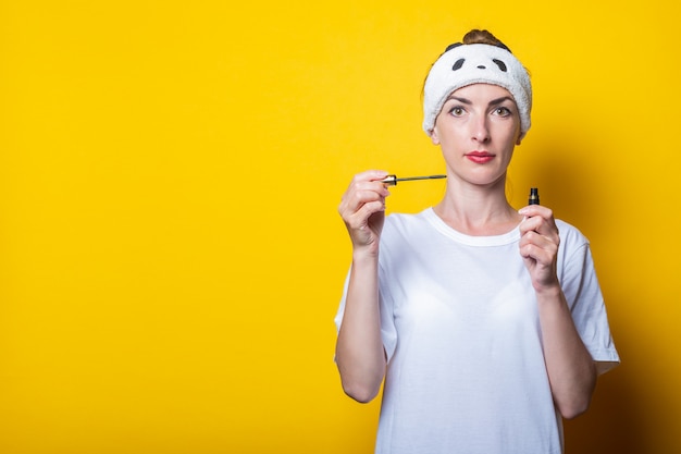 Ragazza che fa trucco. Con in mano un mascara, una maglietta bianca e una benda in testa