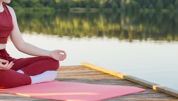 Ragazza che fa yoga sul molo in legno in riva al lago in estate