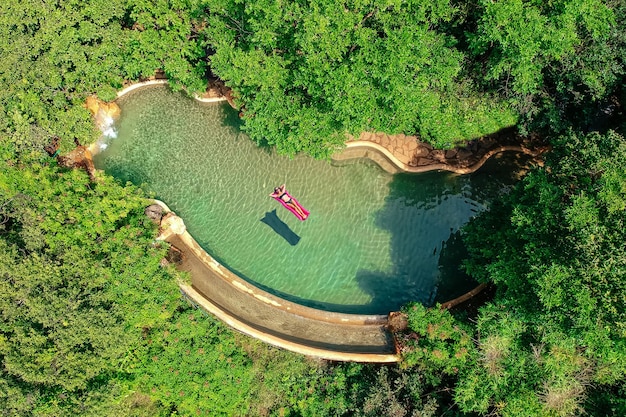 Ragazza che galleggia nell'acqua della piscina rilassante sul materasso gonfiabile rosa in piscina blu lavoro a distanza e vista dall'alto freelance green tree luxury eco hotel a Goa India