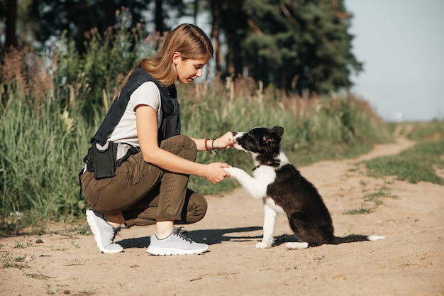 Ragazza che gioca con il cucciolo di cane border collie bianco e nero sulla strada forestale