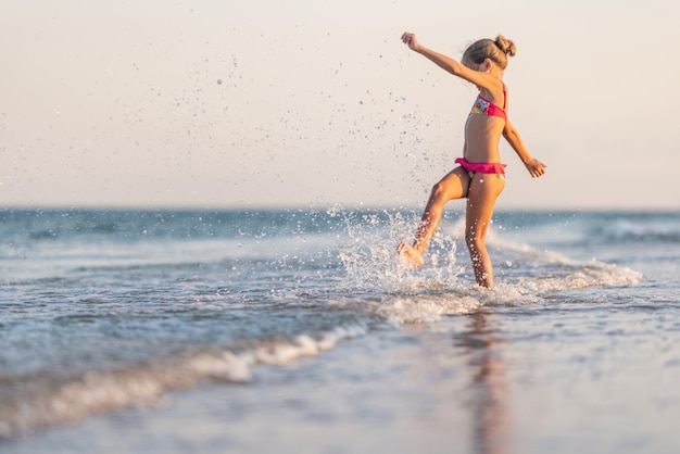 Ragazza che gioca con le onde che scalciano e girano sotto il sole estivo godendosi la vacanza