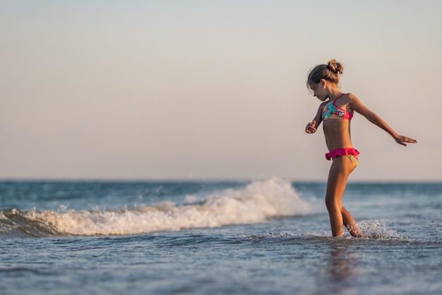 Ragazza che gioca con le onde che scalciano e girano sotto il sole estivo godendosi la vacanza