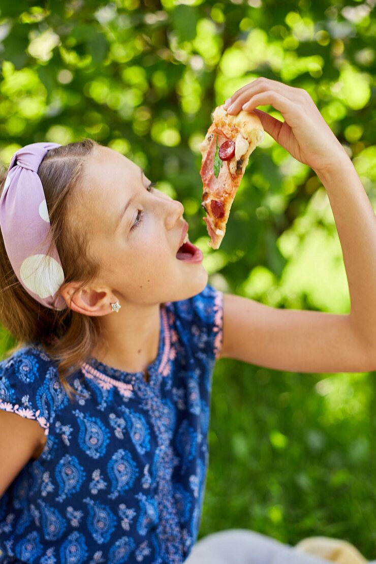 Ragazza che gode di una fetta di pizza all'aperto in una giornata di sole
