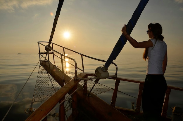 Ragazza che guarda l'alba al mare da una barca a vela