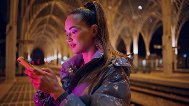 Ragazza che guarda lo schermo di uno smartphone in una città notturna con un primo piano dell'architettura gotica