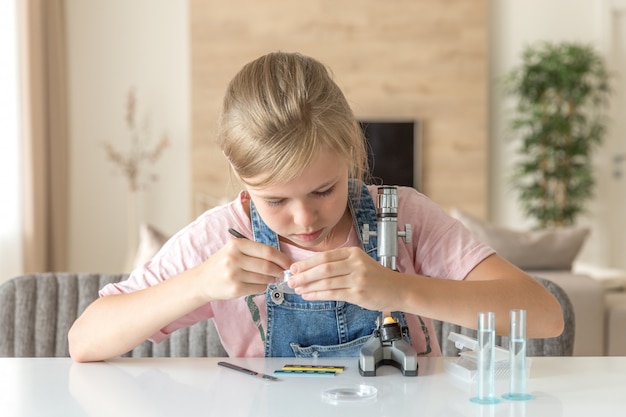 Ragazza che impara chimica che gioca con il microscopio a casa