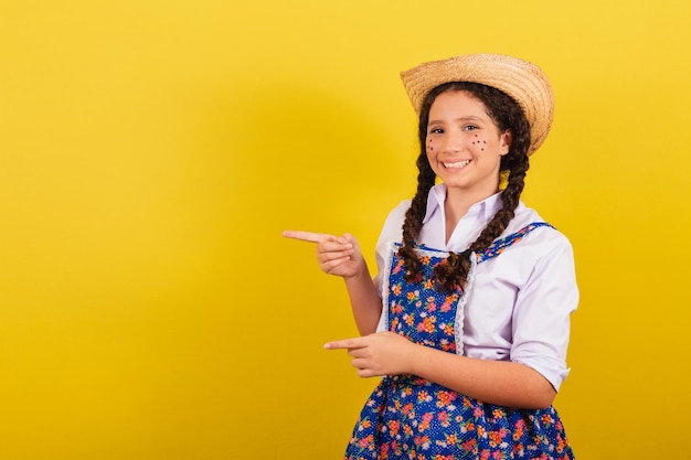 Ragazza che indossa abiti tipici per Festa Junina che indica di lato con le dita spazio per annuncio e testo Per la festa di Arraia