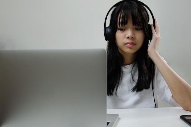 Ragazza che indossa le cuffie che studia online con il computer portatile e ascolta musica rilassante o riproduce i social media su Internet a casa