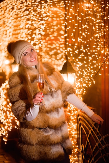 Ragazza che indossa un cappello invernale alla moda con un bicchiere di champagne alla festa durante le vacanze incandescente sfondo oro.
