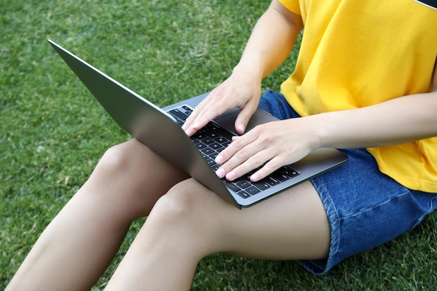 Ragazza che lavora al computer portatile e che si siede sull'erba all'aperto