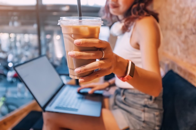 Ragazza che lavora o impara sul computer portatile in un bar o coworking e beve caffè freddo