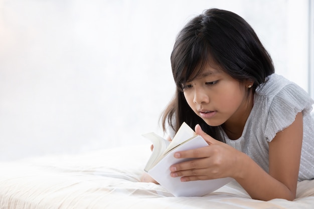 Ragazza che legge nel suo letto accanto alla finestra