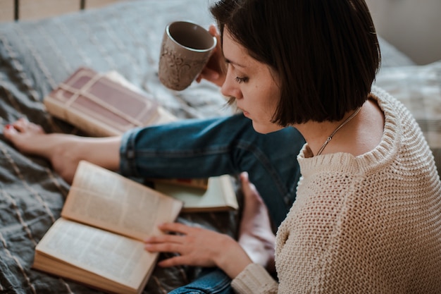 Ragazza che legge un libro e che beve i piedi del caffè a letto sul muro.