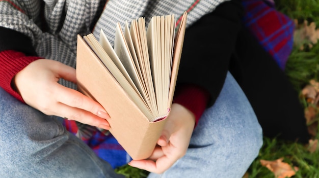 Ragazza che legge un libro nel parco autunnale. Le mani femminili aprono le pagine di un libro di carta all'aperto in una calda giornata di sole. Lo studente si sta preparando per l'esame. Tempo libero letterario in natura.