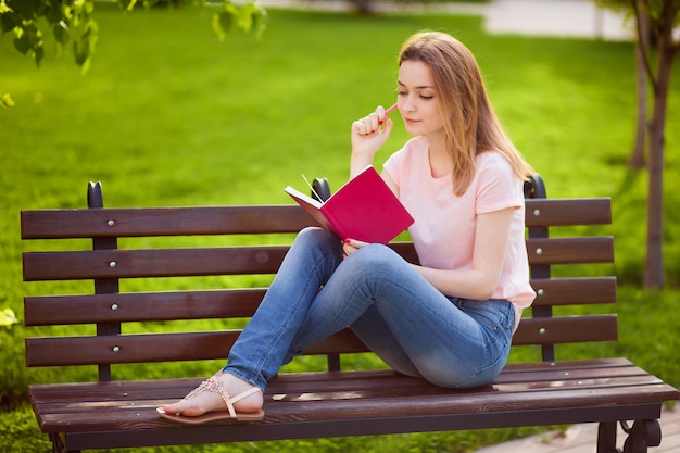 Ragazza che legge un taccuino che si siede su una panchina nel parco