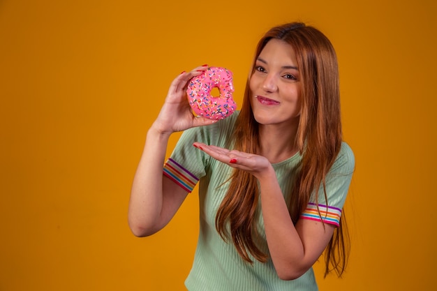 Ragazza che mangia ciambelle rosa su sfondo giallo.