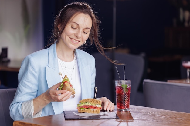 Ragazza che mangia delizioso panino da vicino nella moderna caffetteria