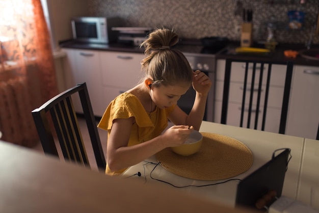 Ragazza che mangia in cucina e guarda video sul ritratto dello stile di vita domestico del tablet