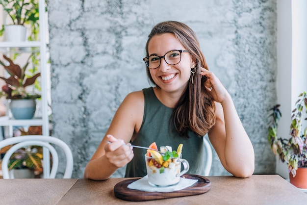 Ragazza che mangia la sua macedonia sana e che guarda l&#39;obbiettivo.