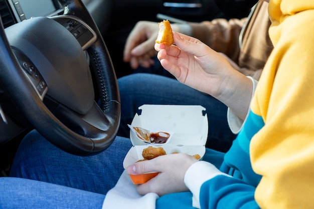 Ragazza che mangia pepite seduta al volante di un'auto Fast food snack da asporto sulla strada